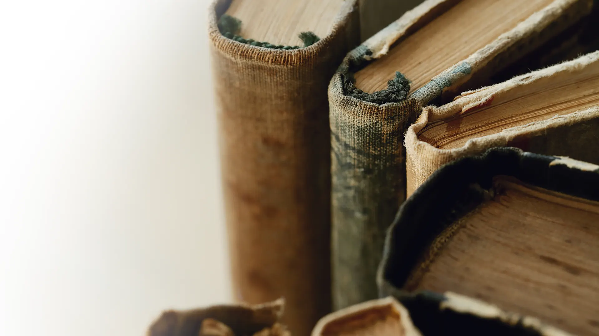 Primer plano de libros antiguos con encuadernaciones de tela desgastadas y lomos deteriorados. Las páginas envejecidas reflejan el paso del tiempo y el uso frecuente. Imagen representativa de la conservación de libros históricos, bibliotecas y archivos patrimoniales.